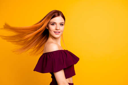 Red straight-haired attractive cute nice cheerful young girl, half turned, wind blowing hair. Isolated over bright vivid yellow backgroundの写真素材