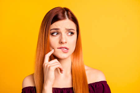 Close up portrait of frustrated confused girl bite her lip and touch cheek by finger isolated on yellow backgroundの写真素材