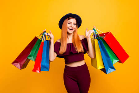 Happy model girl returns from shopping mall holding colorful bags isolated on yellow backgroundの写真素材