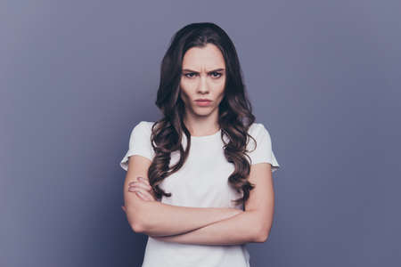 Portrait of pretty stylish nice sad curly-haired girl in casual white t-shirt, crossed hands, isolated over grey backgroundの写真素材