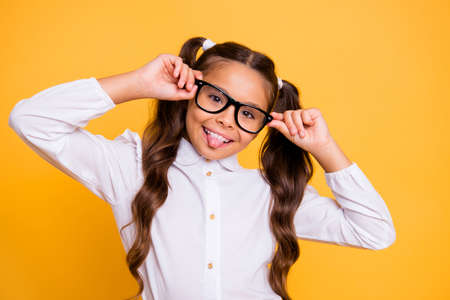 Portrait of cheerful, cute, fun, play, funky, joyful, crazy small girl isolated on vivid yellow background look at camera and show tongue outの写真素材