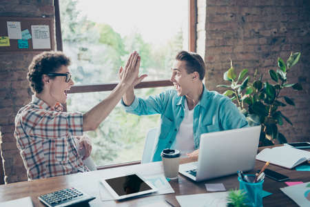 Successful online business project. Two cheerful glad satisfied delighted guys, friends sitting in...