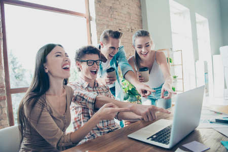 Four cheerful people, friends,  enjoying funny video tutorial, guys and girls pointing with fingers...