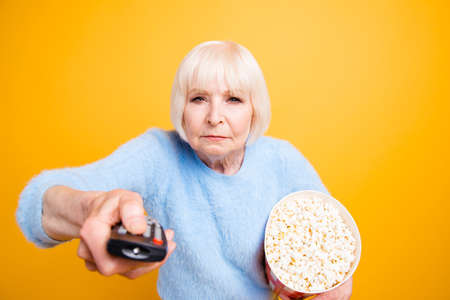 Concentrated old lady with bucket of popcorn switches channels o