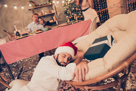 Bearded guy in santa claus cap sleeping on floor, chair near gifの写真素材