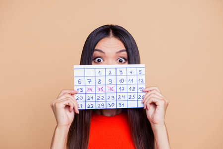 Close up photo portrait of terrified amazed with big eyes lady closing covering she face with paper handmade calendar isolated on pastel beige background copy spaceの写真素材