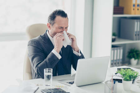 Economist employee manager unsaved man in elegant chic tux trendy formal wear sit on comfort white armchair chair behind desktop with glass water on workstation hold napkin near face close eyesの写真素材