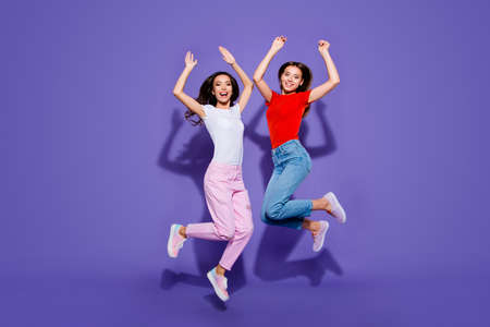 Two charming lovely cute dreamy girls jumping up raising hands isolated violet purple background