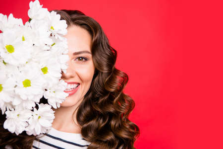 Close-up half-face portrait of nice cute lovely sweet attractive cheerful positive wavy-haired girl hiding holding smelling white flowers isolated over bright vivid shine red backgroundの写真素材