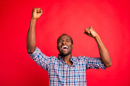Portrait of nice handsome attractive cheerful glad positive guy wearing checked shirt showing breakthrough gesture holding fists raising hands up isolated over bright vivid shine red backgroundの写真素材