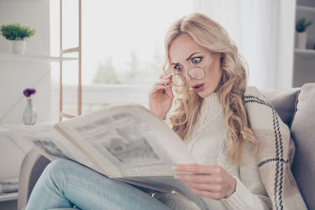 Profile side view portrait of nice adorable attractive intelligent stunned terrified wavy-haired lady wearing sweater holding in hands reading horror stories in light interior roomの写真素材
