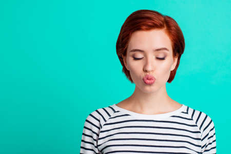 Close-up portrait of her she nice lovely sweet attractive adorable red-haired lady in striped pullover sending air kiss closed eyes isolated over bright vivid shine green turquoise backgroundの写真素材