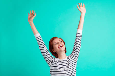 Portrait of her she lovely attractive pretty cheerful optimistic red-haired lady in striped pullover raising hands up having fun isolated over bright vivid shine green turquoise backgroundの写真素材