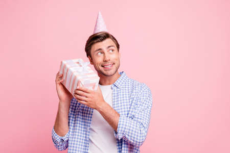 Close up photo of beautiful amazing brunet he him his handsome paper cap on head holding big gift box wondered what inside wearing casual checkered plaid shirt outfit isolated on rose backgroundの写真素材