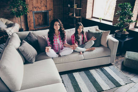 Close up photo calm two people mum little daughter fingers om legs crossed training inner balance lotus pose position wear pink plaid shirts flat apartment room sit folded legs cozy couch sofa divanの写真素材