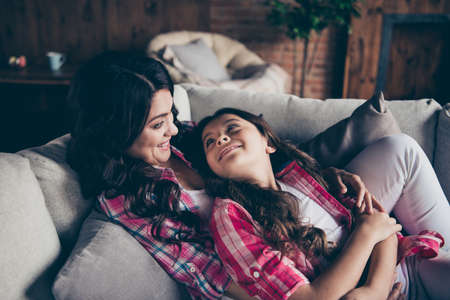 Portrait of two nice cute lovabel winsome attractive lovely cheerful cheery girls wearing checked shirts having fun sitting on divan hugging indoorsの写真素材
