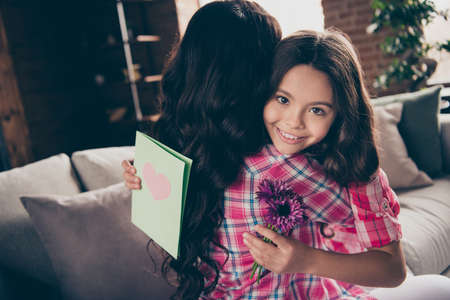 Portrait of nice cute lovely sweet tender gentle attractive charming cheerful cheery positive wavy-haired people girl cuddling dear mom mommy sitting on divan in house indoorsの写真素材