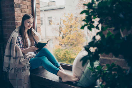 Side profile charming lovely cute nice romantic with long hairstyle one single alone lonely student holding interesting paper book in hands sitting on window-sillの写真素材