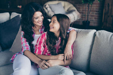 Portrait of two nice stylish trendy sweet attractive lovely winsome tender delicate cheerful wavy-haired girls sisters sitting on divan looking at each other in loft industrial interior indoorsの写真素材