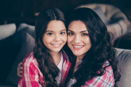 Close up photo two people mum little daughter glad weekend communicate holding hands arms look similar leisure rejoice wear pink plaid shirts jeans bright flat apartment room sit on cozy sofaの写真素材