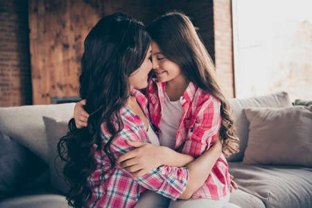 Profile side view portrait of two nice cute attractive lovely lovable charming cheerful cheery people wearing checked shirts cuddling mom mum mommy sitting on divan hugging indoorsの写真素材
