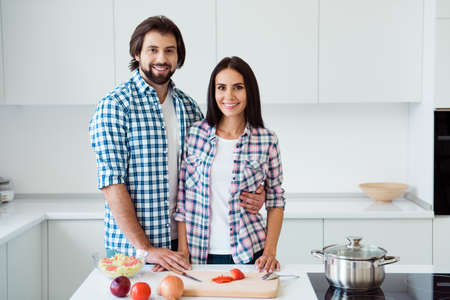 Nice sweet lovely lovable attractive trendy stylish cheerful cheery married spouses making fresh useful healthy dish homemade vegs vegetarian in light white modern interior indoorsの写真素材