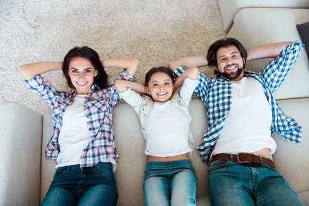 Top above high angle view portrait of nice cool trendy attractive cheerful cheery people mom dad lying on divan having fun free time in light white modern interior indoorsの写真素材