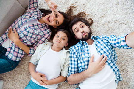 Self-portrait top above high angle view of nice cute charming attractive cheerful cheery foolish dumb people mom dad lying on floor carpet showing v-sign in light white modern interior indoorsの写真素材