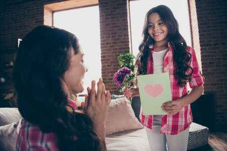 Close up side profile view photo two people mum clap little daughter bouquet postcard present holiday morning unexpected delighted wear pink plaid shirts flat apartment room sit cozy couch sofa divanの写真素材