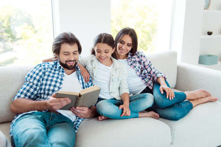 Portrait of nice cute lovely trendy attractive cheerful cheery people mom dad sitting on divan reading free time in light white modern interior indoorsの写真素材