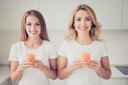 Close up photo two people mum and teen daughter enjoy spending time make vegetables juice health care food eat wear white t-shirts jeans in bright flat kitchenの写真素材