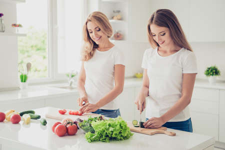 Close up photo two people mum and teen daughter house work duties secrets wisdom of making dishes cook tricks simple tasty cooking study lesson advice wear white t-shirts jeans in bright flat kitchenの写真素材