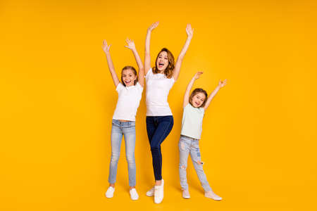 Full length body size portrait of three nice lovely slim attractive cheerful cheery positive ecstatic people having fun raising hands up isolated over bright vivid shine yellow backgroundの写真素材