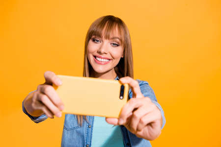 Portrait of her she nice cute sweet lovely attractive winsome cheerful straight-haired lady making taking selfie device gadget isolated over bright vivid shine yellow backgroundの写真素材