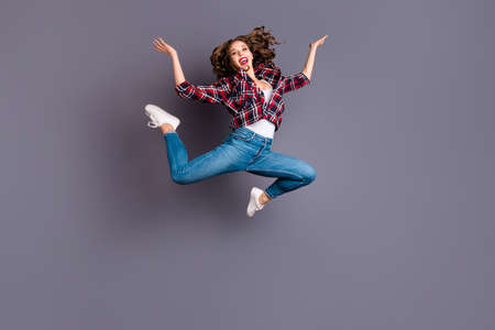 Full length size body view photo jumping high amazing attractive she her lady flight in air legs separate scream shout yell gladly wearing casual jeans denim checkered plaid shirt grey backgroundの写真素材