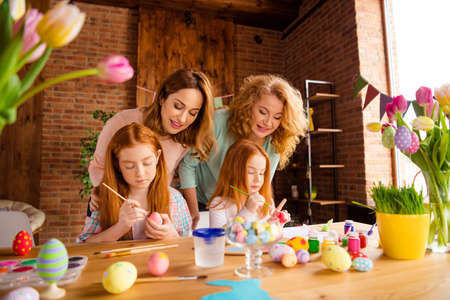 Portrait of two nice attractive cheerful ladies helping assisting two girls doing decorative things dying eggs in house brick loft industrial interior room indoorsの写真素材