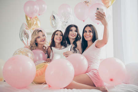 Portrait of nice cute lovely attractive charming cheerful glad girlfriends making taking selfie hugging baloon having fun in light white interior decorated house indoorsの写真素材