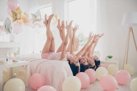 Profile side view of nice winsome lovely attractive cheerful cheery dreamy optimistic girlfriends having fun lying on bed raising legs hands up in light white interior decorated houseの写真素材