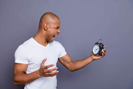 Close up side profile photo sick mad unhealthy dark skin he him his macho bald head puzzled hold clock hopelessness despair yell loudly wearing white t-shirt outfit clothes isolated grey backgroundの写真素材