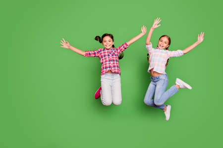 Full length body size photo two little age she her girls hand arm up jump high school competition cheerleaders wear casual jeans denim checkered plaid shirts isolated green vibrant vivid backgroundの写真素材