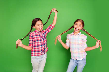 Portrait of two nice sweet cute lovely funny cheerful cheery positive pre-teen girls wearing checked shirt having fun playing with tails isolated over bright vivid shine green backgroundの写真素材