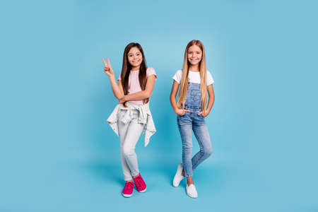 Full length body size view portrait of two people nice lovely charming attractive cheerful straight-haired pre-teen girls siblings showing v-sign isolated on blue turquoise backgroundの写真素材
