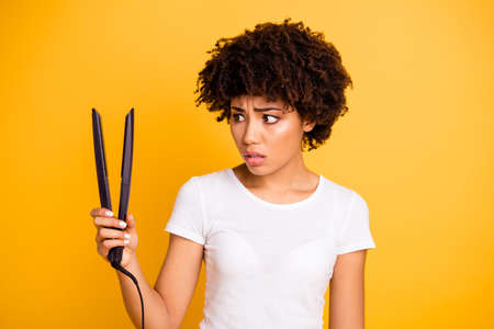 Close-up portrait of her she nice cute lovely charming attractive nervous unsure scared wavy-haired lady holding in hands looking at curling iron isolated on bright vivid shine yellow backgroundの写真素材