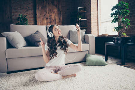 Close up portrait beautiful brunette she her lady singing songs homey watch read song text telephone legs crossed having fun free time wearing sporty domestic light color clothes outfit comfy divanの写真素材