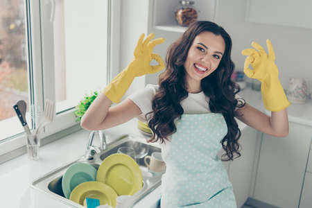 Portrait of her she nice adorable winsome charming attractive beautiful cheerful optimistic wavy-haired house-wife showing two double ok-sign in yellow gloves in modern light white interiorの写真素材