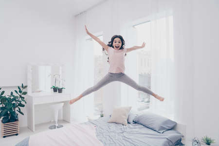 Full length body size view photo funky careless she her little girl jumping high on bed star shape figure form playful wear home t-shirt pants comfortable apartments flat bright light colored roomの写真素材