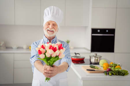 Close up photo funny grey haired he his him grandpa hands arms holding flowers meet ladies 8 march wear chefs white costume uniform casual checkered plaid shirt jeans denim outfit house kitchenの写真素材