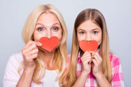 Close up photo funky blond hair she her granny little small granddaughter hide mouth paper heart figure handmade postcard parents wear pink plaid checkered shirt sweater isolated grey background.の写真素材