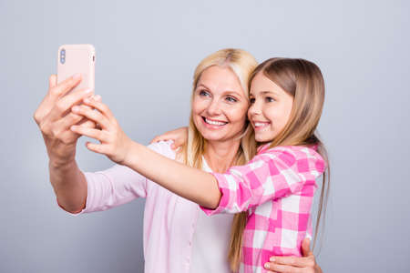 Close up photo cheer two people blond haired she her granny little daughter hold telephone make take selfies weekend wear pink plaid checkered shirt sweater pullover isolated light grey backgroundの写真素材