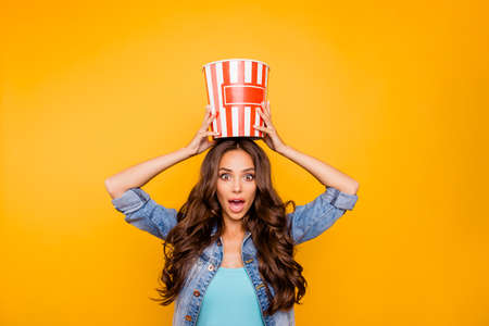 Close up photo beautiful her she lady hold big large popcorn box on head stupor oh no expression change channel wear blue teal green short dress jeans denim jacket clothes isolated yellow backgroundの写真素材